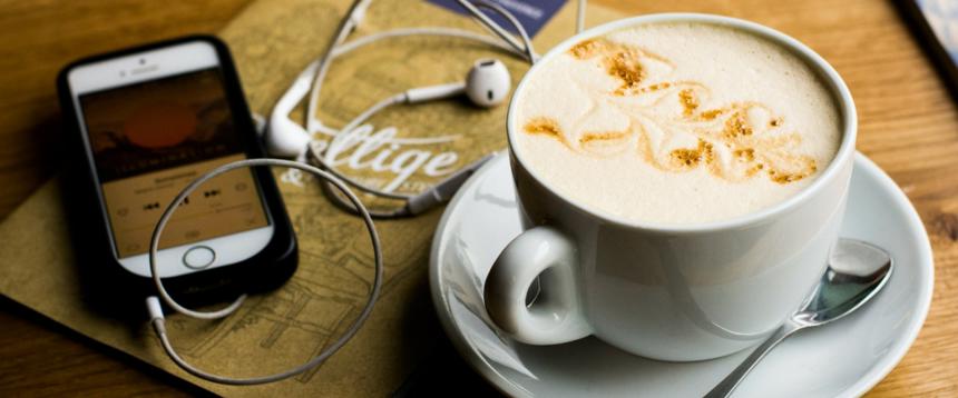 Photo of iPhone and headphones next to a cup of coffee