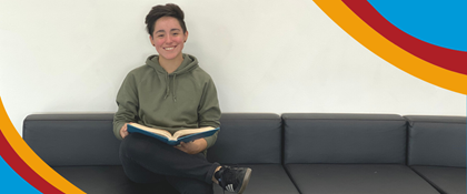 Photo of teen sitting on couch holding a book and smiling