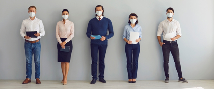 5 people lined up wearing masks and holding papers or folders.