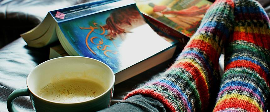 Photo of feet up on couch in colorful socks next to book and cup of coffee.