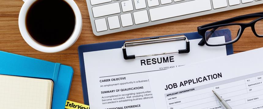 Resume on clipboard, job application, computer keyboard, glasses, notebook and cup of coffee