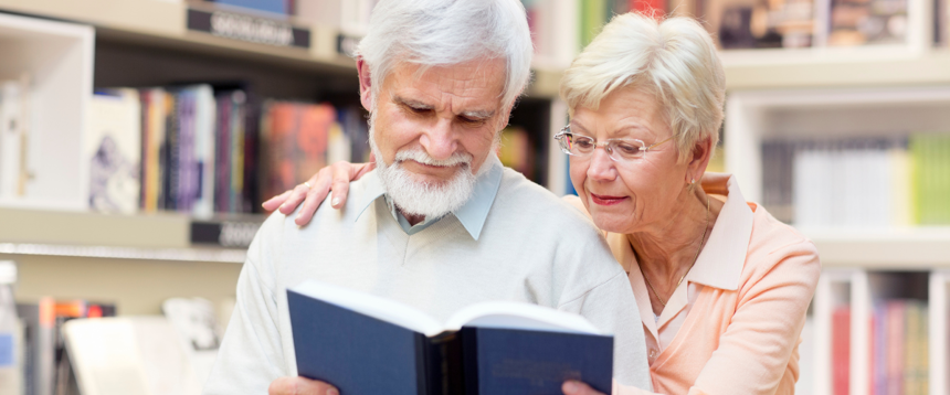 Senior man and woman sitting and reading a book together, with bookshelves in the background