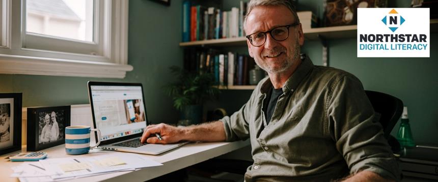 A man sitting at a desk in his home with his laptop open and the Northstar Digital Literacy logo in the top right corner