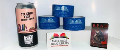 Kombucha can with the words "To Chai For" and the Zip Kombucha Logo, rolls of Anchorage Public Library Duct tape, and the Anchorage Public Library Logo and Baby Yoda Library cards
